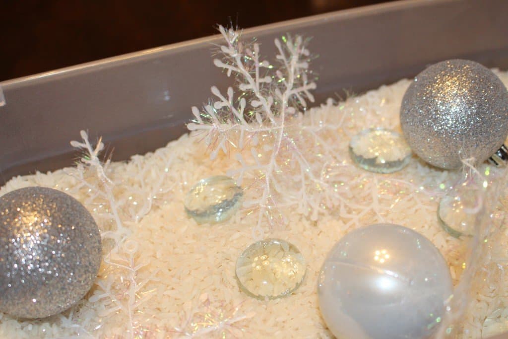 shimery Christmas balls, glass beads and plastic snowflakes laying on top of a bin of rice