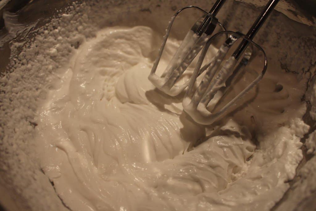 coconut cream being whipped with a handmixer in a stainless steel bowl to make peppermint bark popsicles