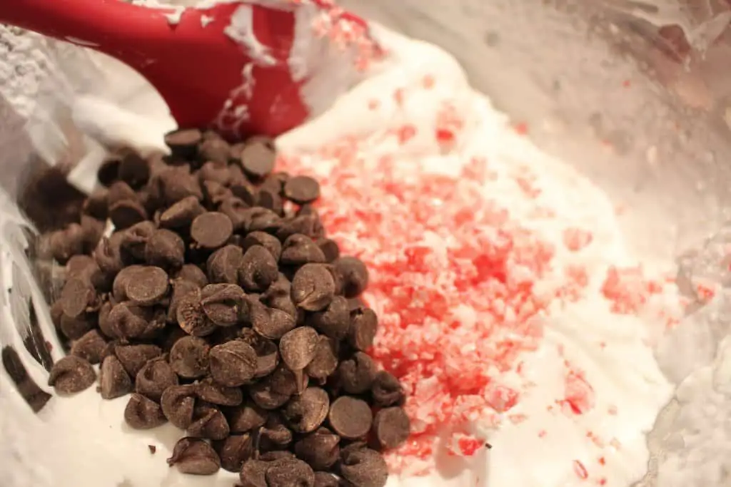 chocolate chips, candy cane chunks, and whipped coconut cream waiting to be mixed together in a stainless bowl