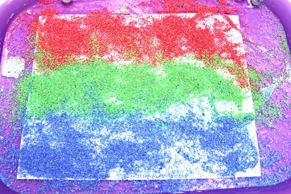 glue covered paper completely covered with a layer of colored craft sand on top