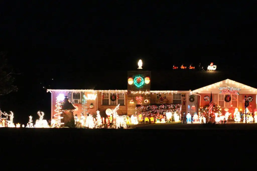 Christmas light display with a lighted green wreath on the chiimney and blow molds in the yard. 