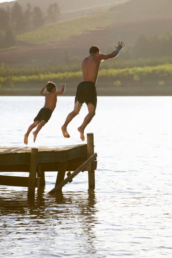 Father adn son jumping off lake dock representing summer activities in Knoxville TN