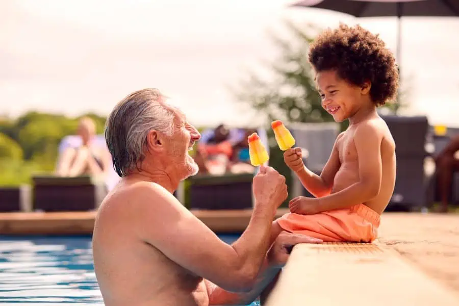 Happy granfather and grandson eat ice pops in a pool.