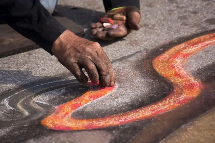 mans hand drawing a chalk mural on the sidewalk.