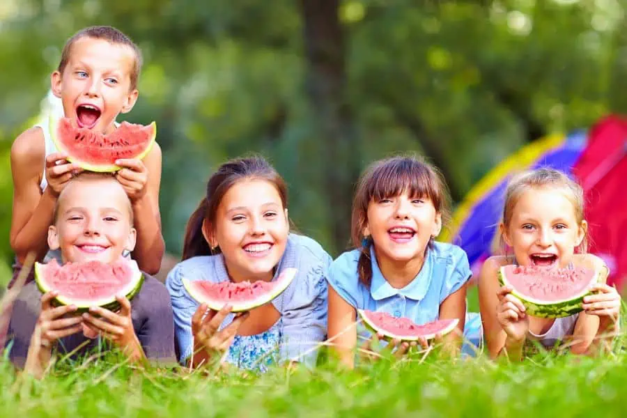a group of kids smiling and eating watermelon. 
