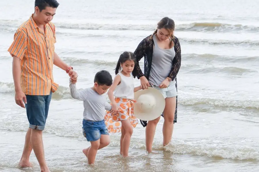 Happy family walking barefoot through beach waves along the shore