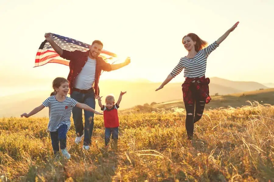 Happy family running in a mountain field holding an American Flag representing things to do in Knoxville in July
