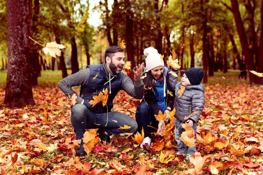 Happy family wearing jackets and playing in fall leaves representing things to do in Tri-Cities TN in October