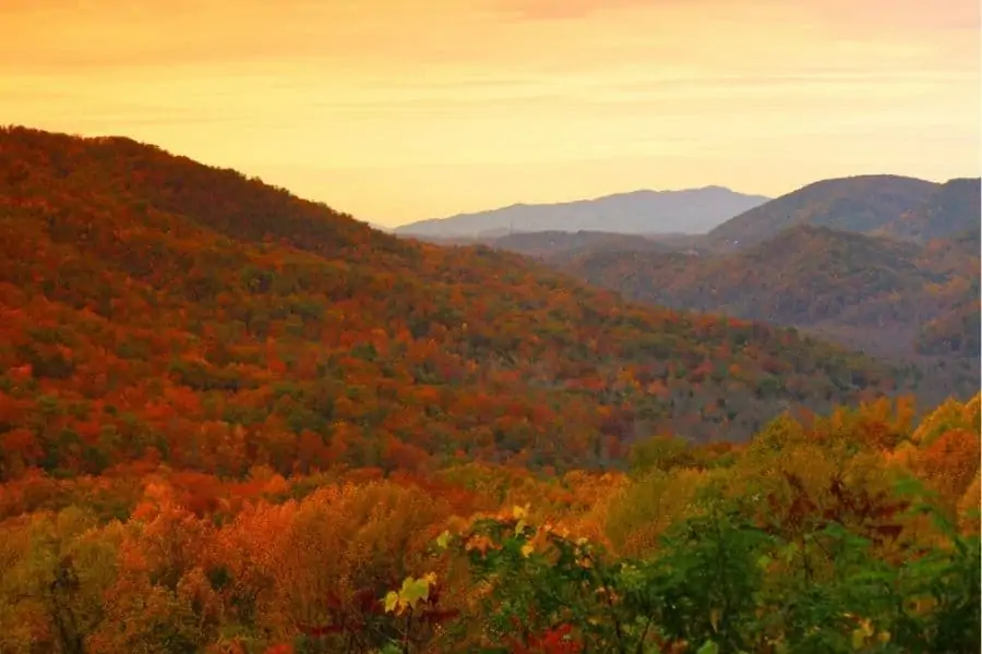 gorgeous mountains with bright fall colors set against a orange hued sky 