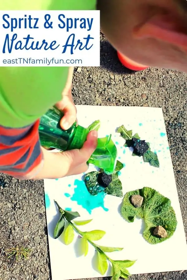 child spraying green color onto a white paper covered with leaves and rocks