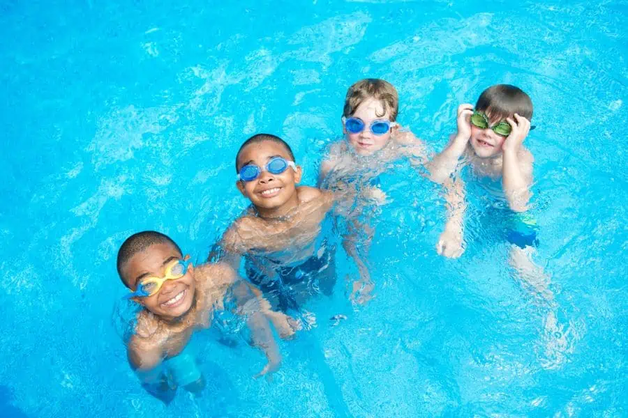 4 happy boys swimming in a pool with goggles on representing indoor pools in Chattanooga TN.