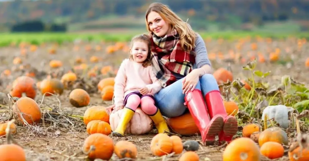 Excited mother and daughter posing for a family photo in a pumpkin field. 