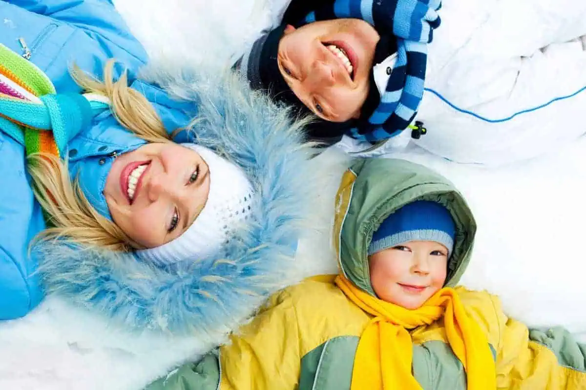 A happy family laying together on the snowy ground enjoying a winter in East Tennessee.