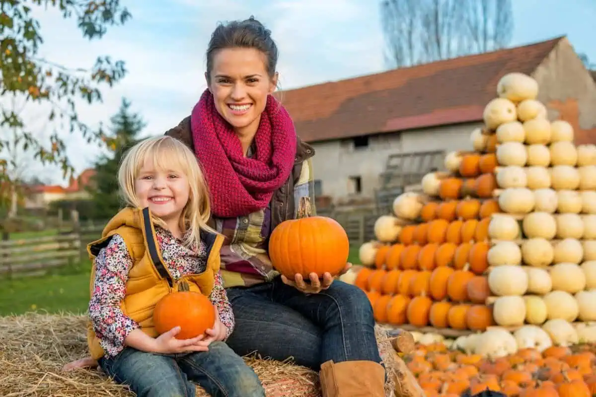 A happy mother and daughter siting in front of a pyramid of pumpkins, representing fall festival in Johnson City TN.