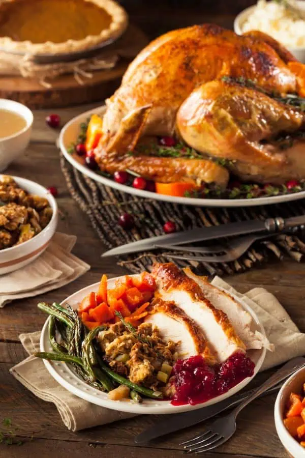 A plated Thanksgiving meal on the table in front of a whole roasted turkey. 
