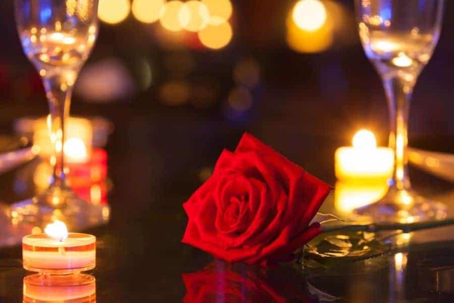 a rose sitting on a candlelit table with chanpange glasses