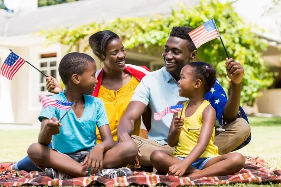 Happy black family sitting on lawn holding American flags, representing July 4th events in Knoxville.