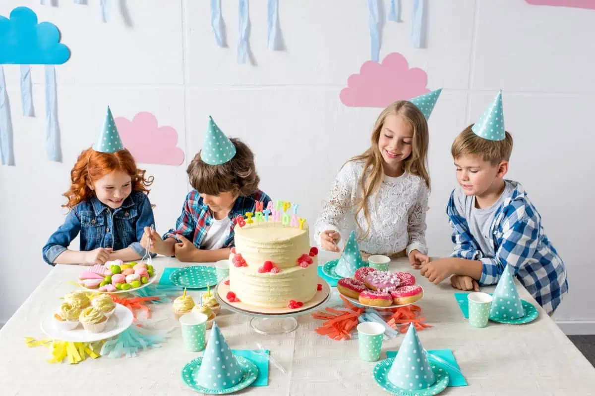 4 happy children gathering around a cake at a weather themed birthday table, representing birthday party venues in Knoxville TN.